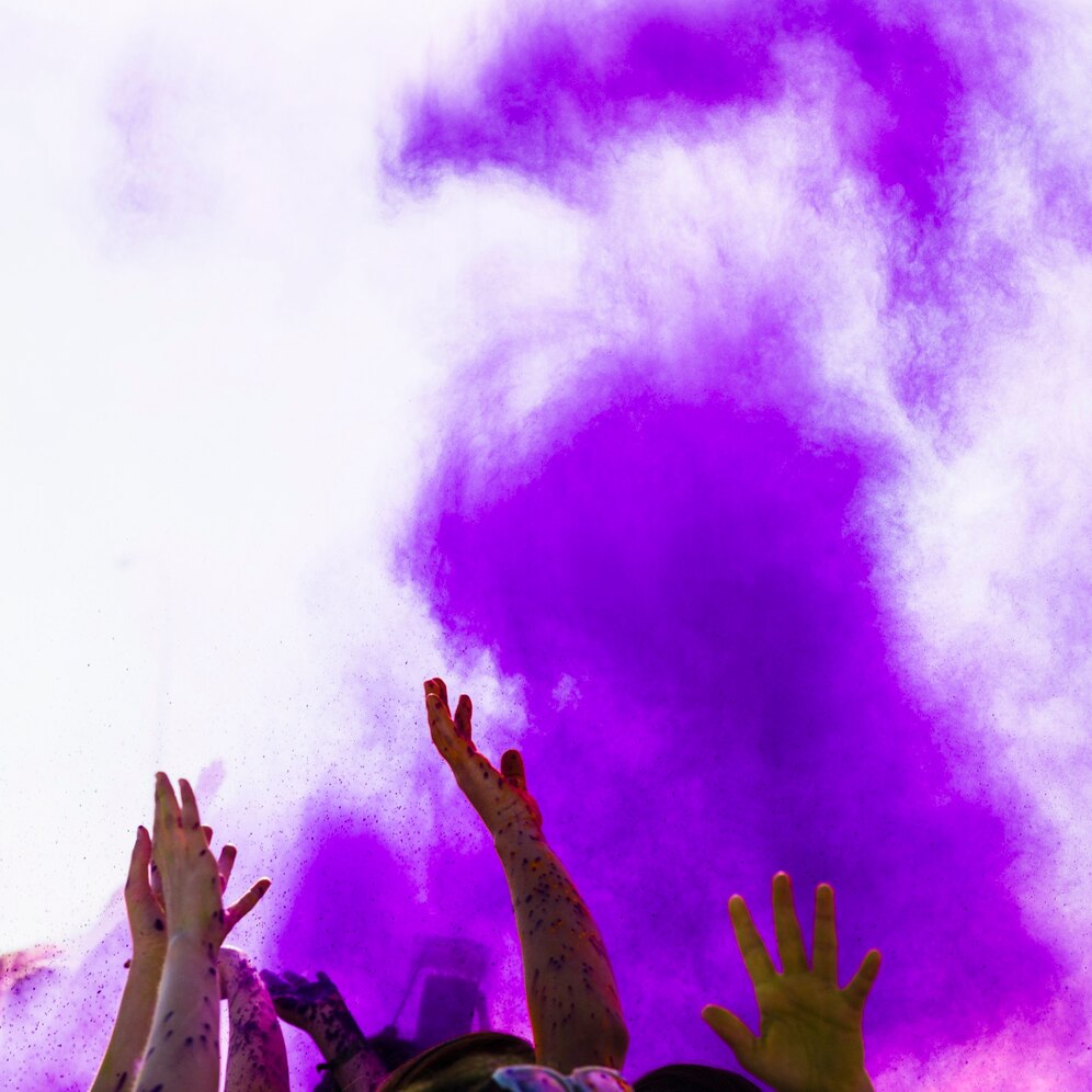 color-holi-morado-sobre-personas-levantando-sus-manos-bailando_23-2148129376